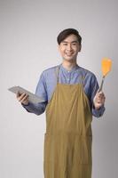 Portrait of young asian man wearing apron holding tablet over white background studio, entrepreneur concept photo