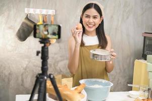 Beautiful woman is making bakery while live streaming or recording video on social media in her house, coffee shop business concept. photo