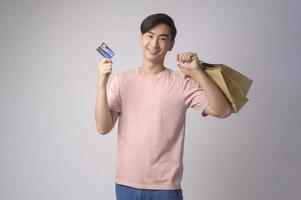 Young asian man holding credit card and shopping bag over white background studio, shopping and finance concept. photo