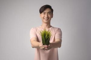 Young smiling man holding tree over white background studio, save earth concept photo