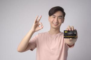 Young asian man holding credit card over white background studio, shopping and finance concept. photo