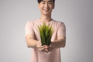 Young smiling man holding tree over white background studio, save earth concept photo