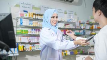 Una farmacéutica musulmana que asesora a una cliente sobre el uso de medicamentos en una farmacia moderna. foto