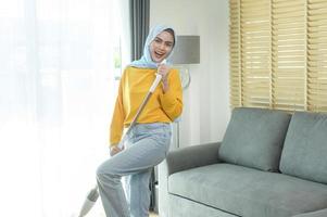 Young happy muslim woman mopping and vacuum the floor in living room. photo