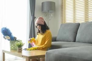 joven mujer feliz con guantes amarillos y quitando el polvo de la mesa en la sala de estar. foto