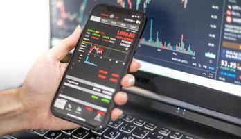 Female trader investor broker analyst holding a smartphone in hand analyzing stock market trading charts indexes data checking price using mobile stock market exchange application. photo