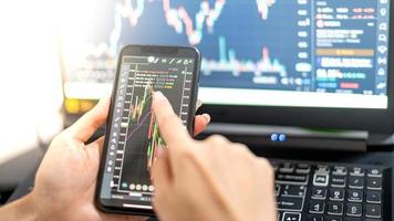 Female trader investor broker analyst holding a smartphone in hand analyzing stock market trading charts indexes data checking price using mobile stock market exchange application. photo