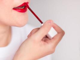 A hand of woman dyeing the lips with red lipstick. photo