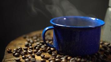 chicco di caffè sul vecchio pavimento di legno e una tazza di caffè smaltata con fumo. set di caffè con bricco. video