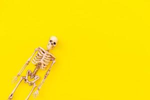 Halloween minimal decorations, composition with spooky skeleton monster isolated on yellow background. Halloween celebration trick or treat concept. Flat lay top view copy space.