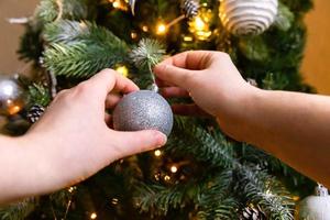 Woman hands decorating Christmas tree. Christmas tree with wite and silver decorations, ornaments toy and ball. Modern classical style interior design. Christmas eve at home, time for celebration. photo