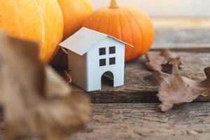 Autumnal Background. Toy house and pumpkin on wooden background. Thanksgiving banner copy space. Hygge mood, change of seasons concept. Hello Autumn with family Halloween party. photo