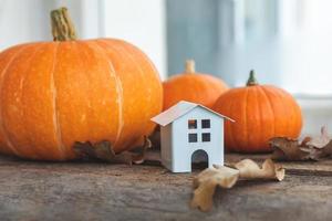 Autumnal Background. Toy house and pumpkin on wooden background. Thanksgiving banner copy space. Hygge mood, change of seasons concept. Hello Autumn with family Halloween party. photo