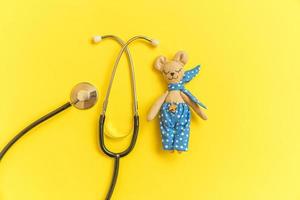 Simply minimal design toy bear and medicine equipment stethoscope isolated on yellow background. Health care children doctor concept. Pediatrician symbol. Flat lay top view layout, copy space photo