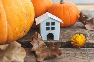 Autumnal Background. Toy house and pumpkin on wooden background. Thanksgiving banner copy space. Hygge mood, change of seasons concept. Hello Autumn with family Halloween party. photo