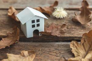 Autumnal Background. Toy house and dried fall leaves on wooden background. Thanksgiving banner copy space. Hygge mood cold weather concept. Hello Autumn with family. photo