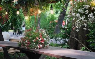 hermoso lugar romántico en el café de la calle en un parque. mesa de madera decorada con flores y cestas de mimbre. lámparas colgadas sobre una mesa. lugar para descansar y tener citas. foto