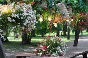 beautiful romantic place at street cafe in a park. wooden table decorated with flowers and wicker baskets. lamps hanging over a table. place for getting rest and dating. photo