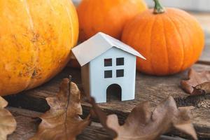 Autumnal Background. Toy house and pumpkin on wooden background. Thanksgiving banner copy space. Hygge mood, change of seasons concept. Hello Autumn with family Halloween party. photo