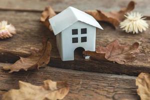 Autumnal Background. Toy house and dried fall leaves on wooden background. Thanksgiving banner copy space. Hygge mood cold weather concept. Hello Autumn with family. photo