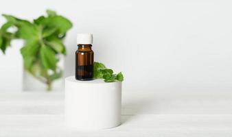 aromatherapy oil in a browm glass bottle on podium with mint leaves. mint and menthol as calm and relaxing fragrances, essential oil for ambient atmosphere. photo