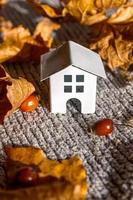 Autumnal Background. Toy house and dried orange fall maple leaves on grey knitted sweater. Thanksgiving banner copy space. Hygge mood cold weather concept. Hello Autumn with family photo