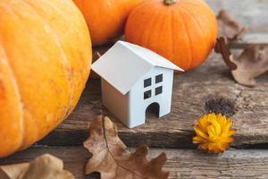 Autumnal Background. Toy house and pumpkin on wooden background. Thanksgiving banner copy space. Hygge mood, change of seasons concept. Hello Autumn with family Halloween party. photo