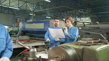 professionele teams van industriële arbeiders in veiligheidsuniformen en ingenieurspartners werkten met metaalbewerkingsgereedschap, bespraken mechanisch tekenen voor draaimachines en werkplaatsen in de productiefabriek. video