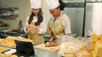 Two female startup chefs live stream via internet online application, demonstrate and show, slice fresh bread with knife in kitchen, pastry cuisine food occupation, social media e-commerce business. video