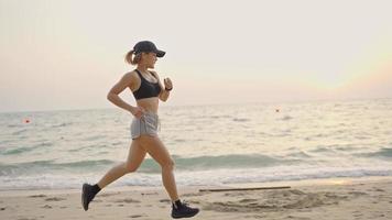 vrouw loopt oceaan strand. jonge Aziatische vrouw die buiten aan de kust traint. concept van gezond hardlopen en buiten sporten. actieve, sportieve atleet joggen. zomer actief video