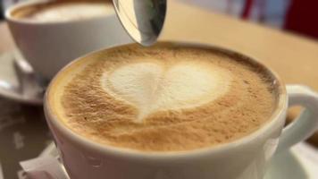 Tasse Cappuccino mit Schaum in Herzform mit einem Löffel gerührt video