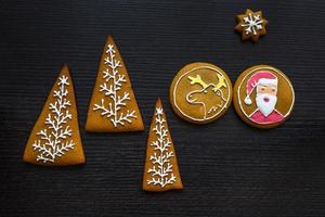 Handmade festive gingerbread cookies in the form of stars, snowflakes, people, socks, staff, mittens, Christmas trees, hearts for xmas and new year holiday on black wooden background photo