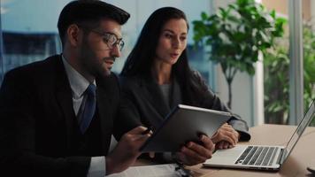 dois colegas discutem dados de análise de marketing usando laptop ou notebook tendo conversa de negócios ajuda colega de trabalho com projeto corporativo sentado na mesa do escritório. video