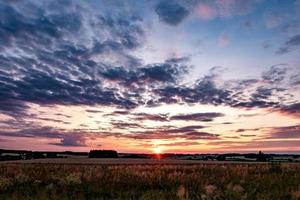 Blue red sky background with evening fluffy curly rolling clouds with setting sun. Good windy weather photo