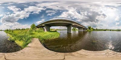 full seamless spherical hdri panorama 360 degrees angle view on wooden pier of shore of wide river near bridge in sunny day with clouds in equirectangular projection, ready VR AR content photo