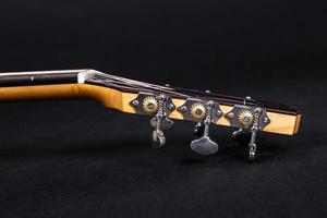 Tuning pegs on wooden machine head of six strings acoustic guitar neck on black background photo