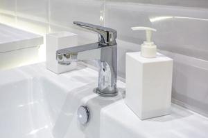 Soap and shampoo dispensers near Ceramic Water tap sink with faucet in expensive loft bathroom photo