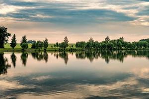 reflejo de los árboles en el agua de un lago en una tranquila tarde de verano foto