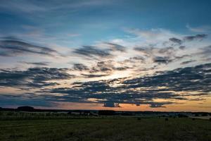 Blue sky background with evening fluffy curly rolling altocumulus altostratus clouds with setting sun. Good windy weather photo