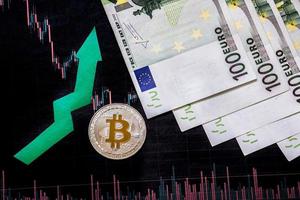 appreciation of virtual money bitcoin. Green arrow and silver Bitcoin on hundred euro bills and paper forex chart index rating on exchange market background. Concept of appreciation of cryptocurrency. photo