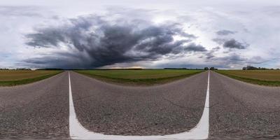 vista de ángulo de 360 grados de panorama hdr esférico completo en carretera asfaltada entre campos por la noche con impresionantes nubes negras antes de la tormenta en proyección equirectangular, vr ar contenido de realidad virtual foto