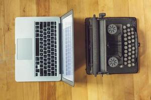 old vintage dust-covered typewriter with sheet of white paper near modern notebook on bookcase background. modern technology and vintage appliances photo