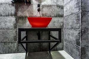 lavabo rojo con grifo en un costoso baño de loft en un bar deportivo de élite con fondo de pared de ladrillo negro foto