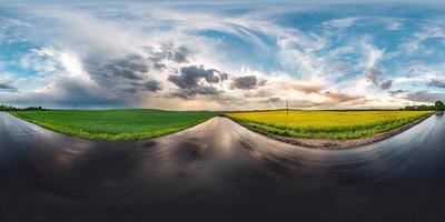 panorama hdri esférico completo sin costuras vista en ángulo de 360 grados en carretera asfaltada húmeda entre campos de canola en la puesta de sol después de la tormenta con nubes impresionantes en proyección equirectangular, contenido vr ar foto