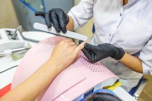 the master in black gloves in the salon makes manicure pedicure to the client photo