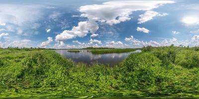 panorama hdri esférico completo sin costuras vista en ángulo de 360 grados en la costa de hierba de un gran lago o río en un día soleado de verano y clima ventoso con hermosas nubes en proyección equirectangular, contenido vr foto