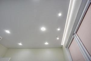 halogen spots lamps on suspended ceiling and drywall construction in in empty room in apartment or house. Stretch ceiling white and complex shape. photo