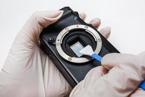 Close-up of mirrorless digital APS-C dirty camera matrix sensor cleaning and maintenance with swab, photographer cleaning photocamera on white background photo