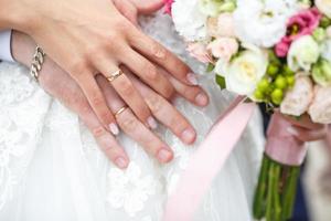 el novio abraza a la novia con un ramo de rosas rojas y blancas. anillos en las manos de la pareja de recién casados foto