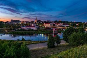 vista panorámica por la noche en el casco antiguo a orillas del río ancho con nubes de cirrostratos ondulantes y rizadas por la noche y el cielo azul violeta rojo de la puesta de sol como fondo foto